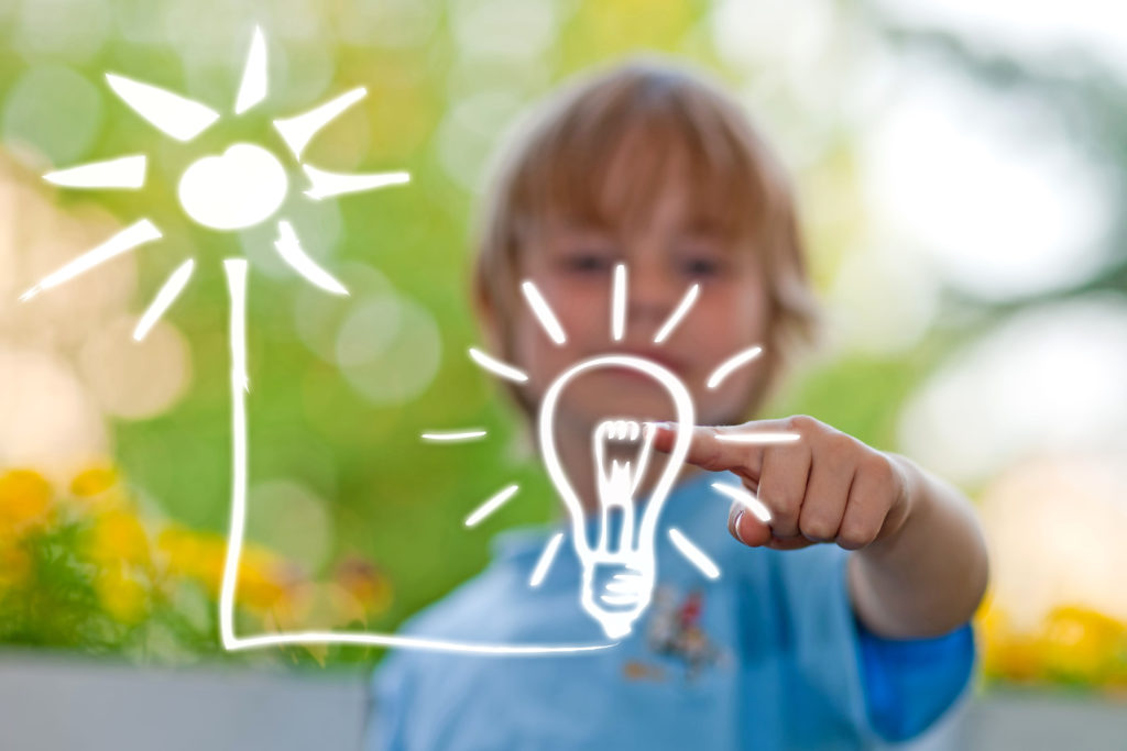 Erneuerbare Energien Anlagen, Ein Junge malt eine Sonne, die mit einer Glühbirne verbunden ist.